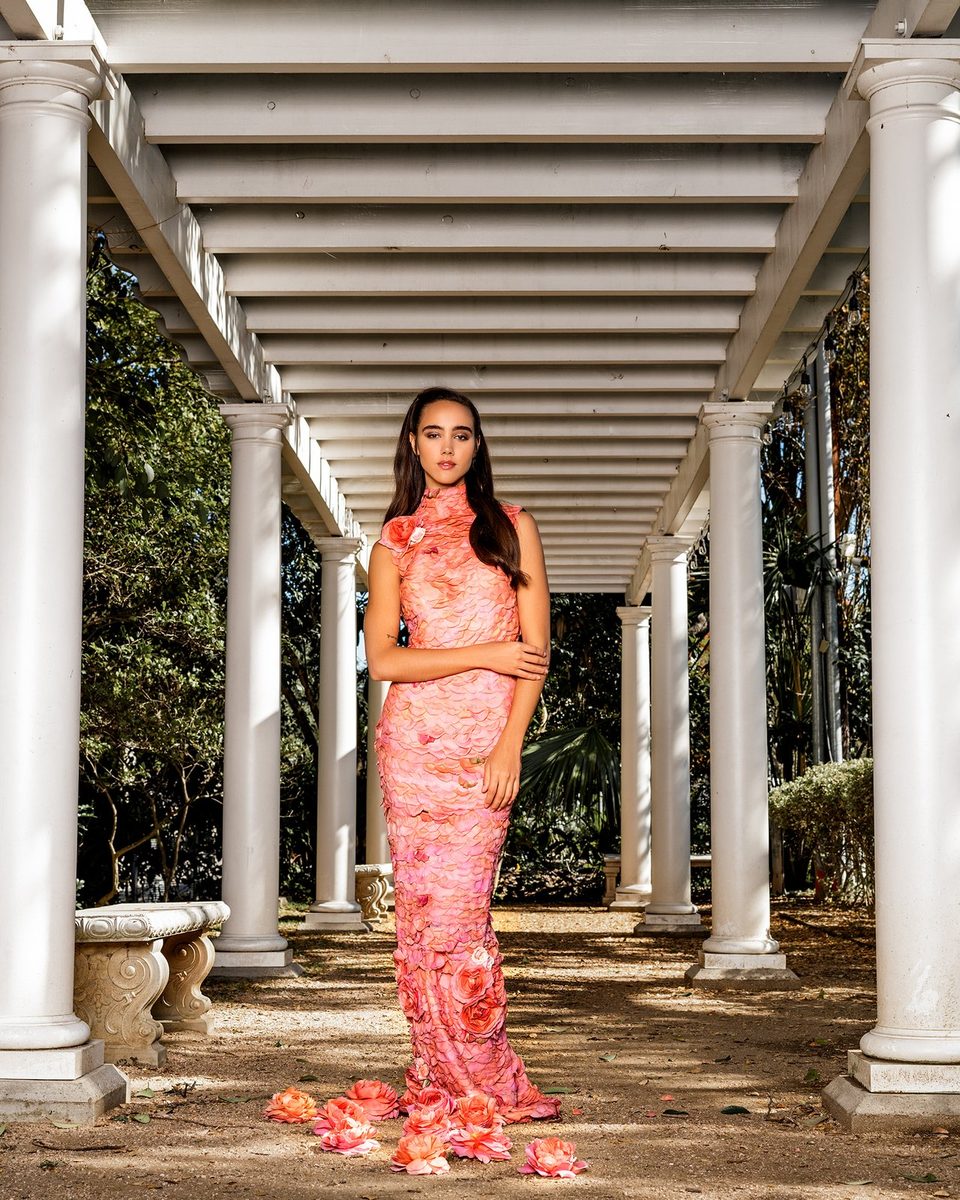 A coral petal gown under a white colonnade.