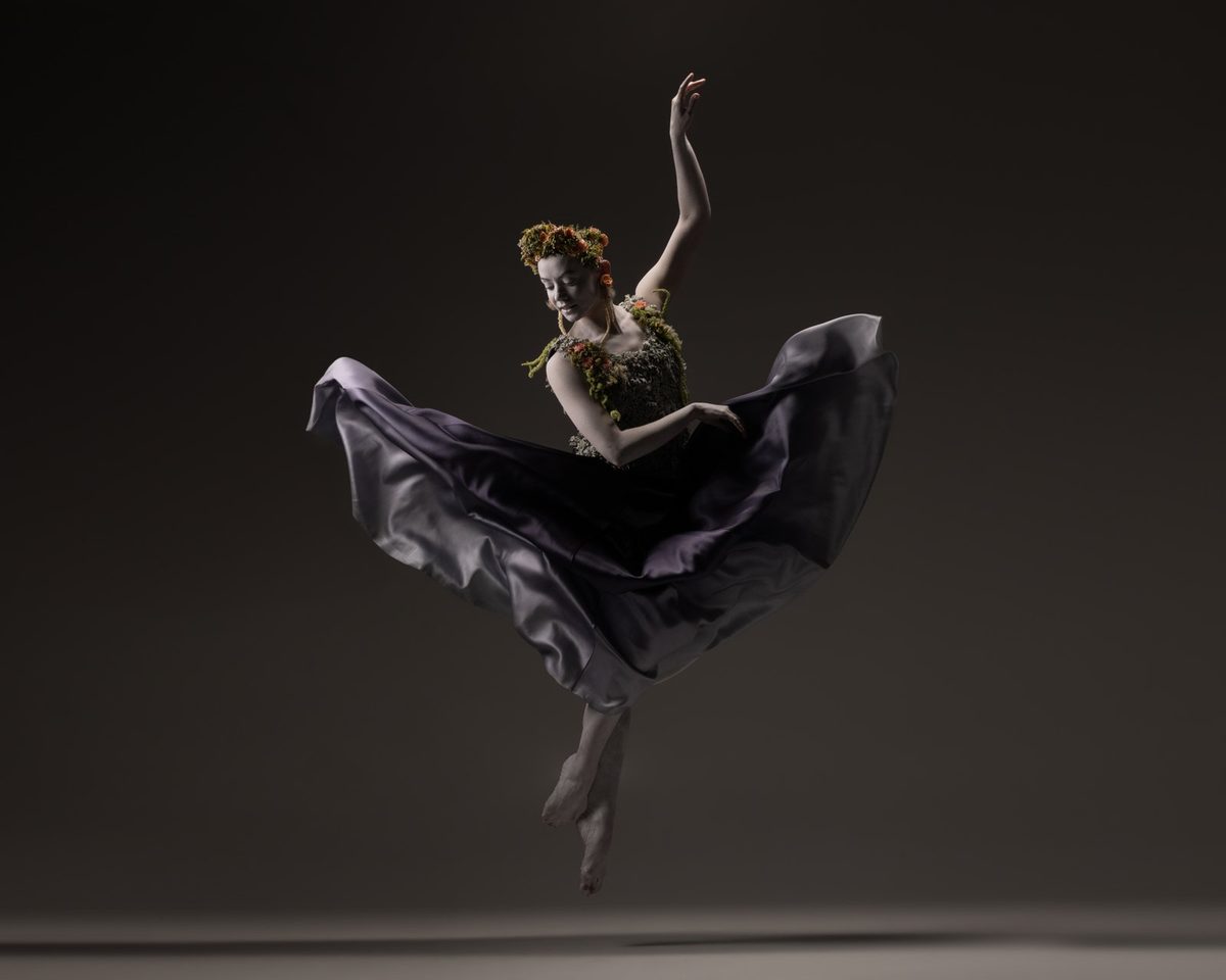 A dancer mid-leap in a dark floral skirt and headpiece.