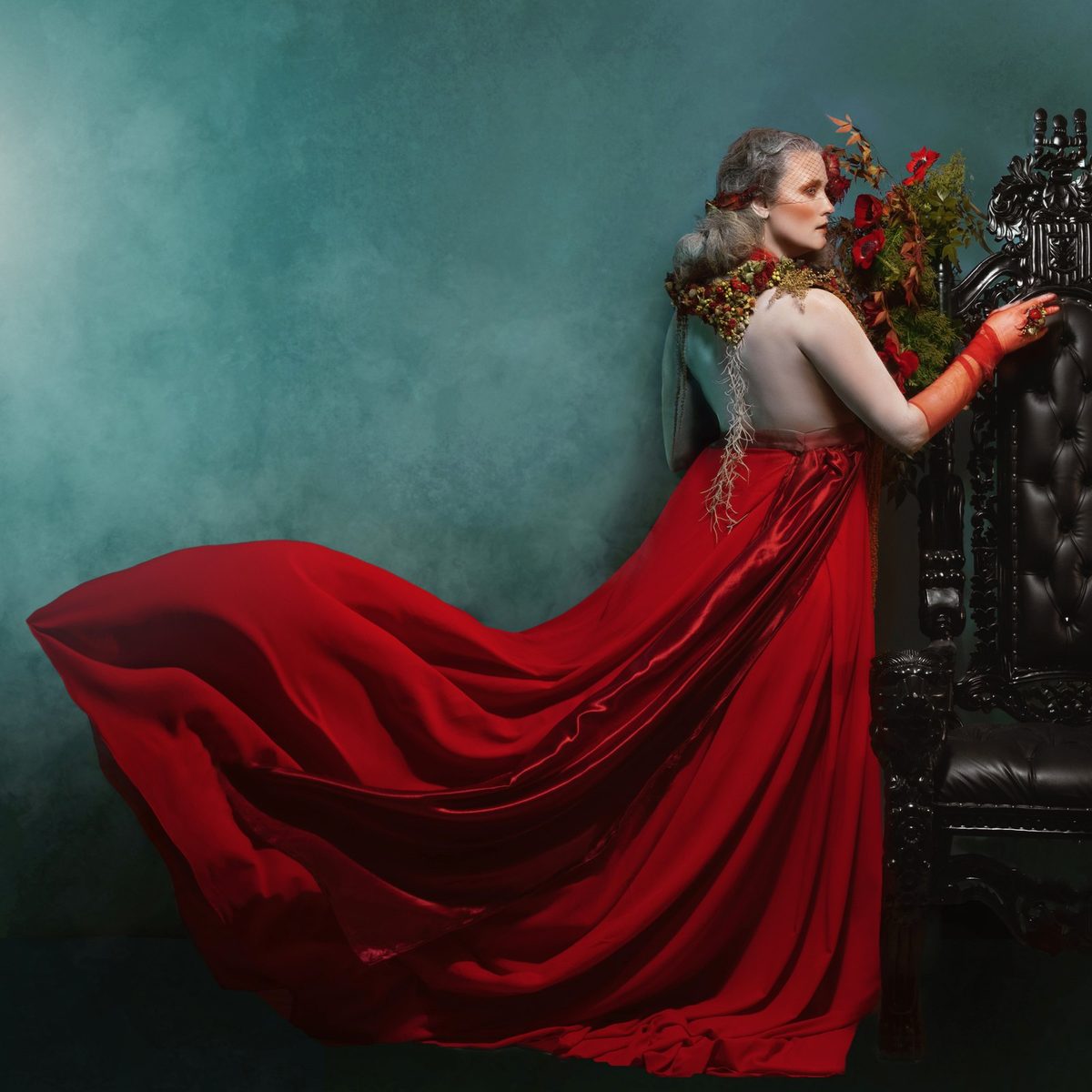 A red gown with a long train beside a carved throne.