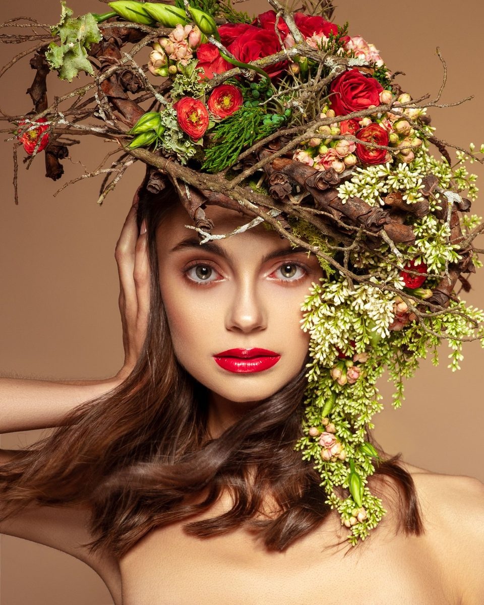 A close portrait under a headpiece of red roses and trailing greenery.