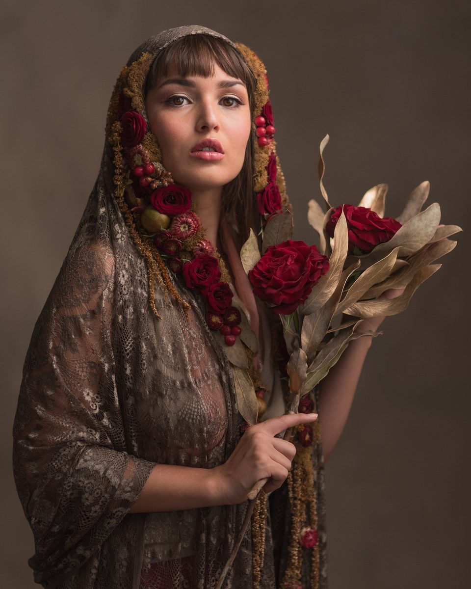 A silk shawl with rose trim. The wearer holds a bouquet of roses and protea.